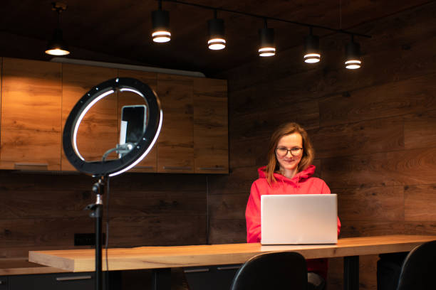Social media influencer creating content at modern studio sharing online stream using smartphone and laptop. Girl blogger smiling and speaking recording video with ring lamp. Online training courses. influencer de redes sociales que crea contenido en un estudio moderno que comparte la transmisión en línea usando un teléfono inteligente y una computadora portátil. chica blogger sonriendo y hablando grabando video con lámpara de anillo. cursos de fo