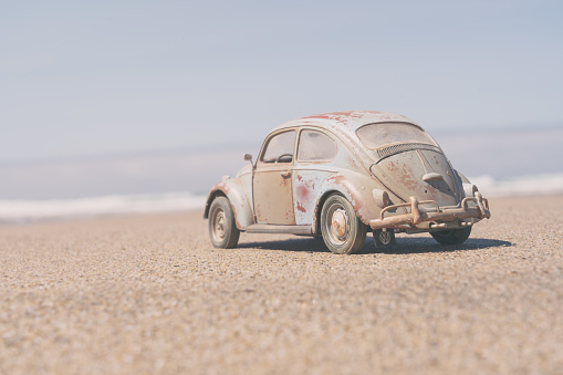 Perranporth, UK - 3rd August, 2022:  A beaten and battered VW Beetle sits on a beach in Cornwall with the summer sunshine beating down on its faded paintwork. Scale model photography.