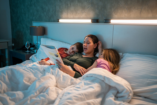 Mother reading bed time stories to her young son and daughter, while they are all lying in bed.