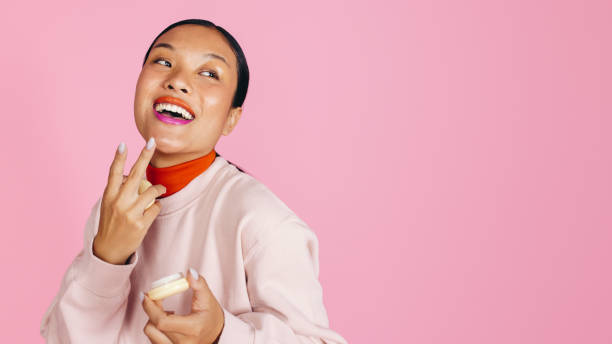 Happy woman applying cream foundation to her face in a studio
