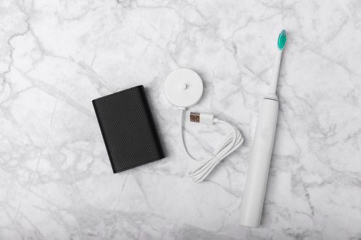 A modern electric toothbrush is charged from an external power bank battery on a marble background. Smart electric toothbrush on a pink background.Modern technologies for health. Healthy teeth.