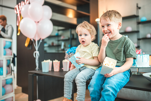 The special bond between two adorable brothers enjoying popcorn and surrounded by festive decorations at a gender reveal party.