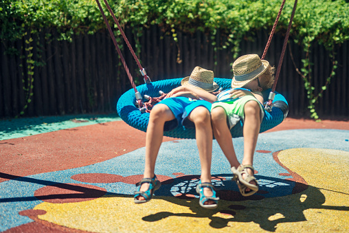 Two boys on a lazy, hot summer day. Kids are lying on on a big swing on the playground and sleeping.\nNikon D810