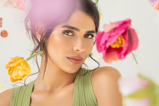 Studio shot of a beautiful natural brunette with perfect skin. Natural sunlight. Flowers floating around her.