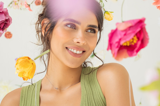 Studio shot of a beautiful natural brunette with perfect skin. Natural sunlight. Flowers floating around her.