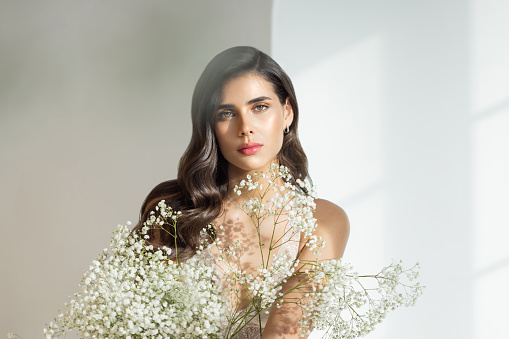Studio shot of a beautiful natural brunette  woman with perfect skin. Natural sunlight. Holding flowers.