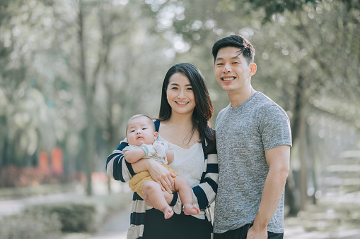 Asian Chinese Parents and baby boy looking at camera smiling in public park during weekend morning