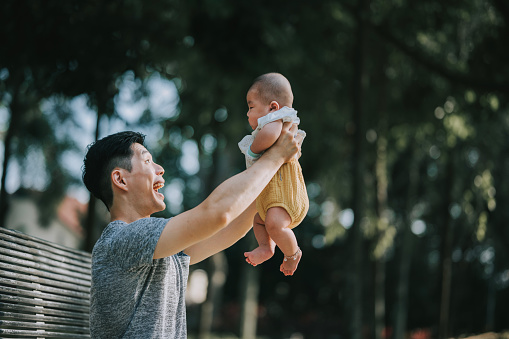 Asian Chinese Father lift up playing with baby boy at park. Young asian father holding his baby son aloft in park or garden with happy emotion
