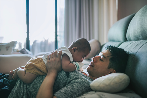 Cozy moment Asian Chinese father lying on bed playing with baby boy weekend morning