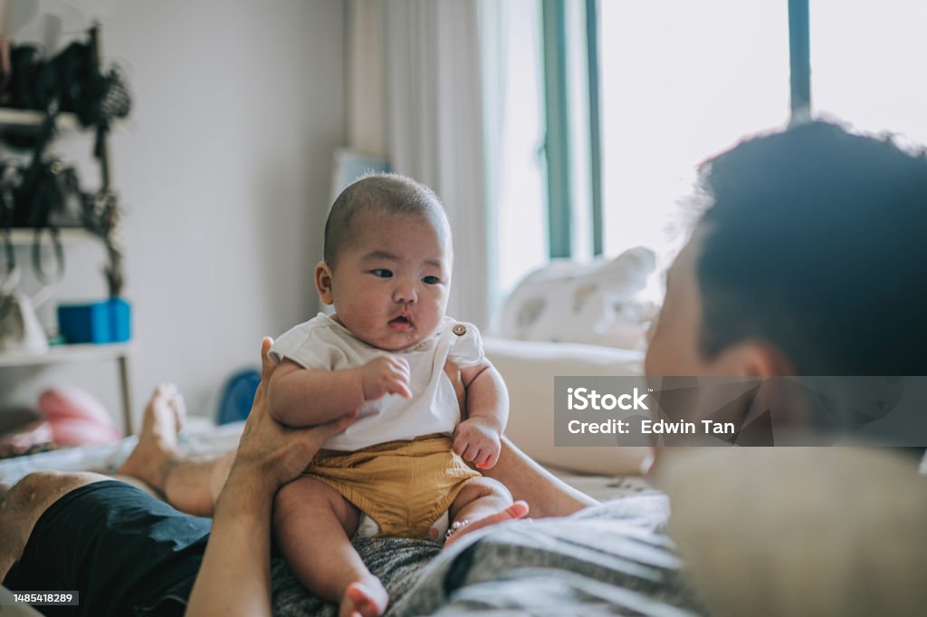 Asian Chinese baby boy sitting on father's abdomen on bed weekend morning Bed - Furniture Stock Photo