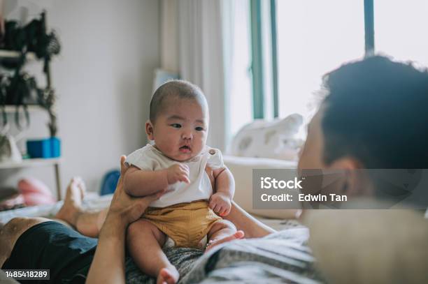 Asian Chinese Baby Boy Sitting On Fathers Abdomen On Bed Weekend Morning Stock Photo - Download Image Now