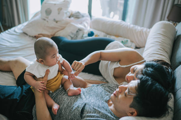 asiatische chinesische eltern, die sich am wochenendmorgen zusammen mit ihrem kleinen jungen auf das bett legen - women group of people lying down mother stock-fotos und bilder