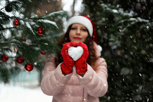 a girl in a Santa Claus hat and red gloves near a decorated Christmas tree