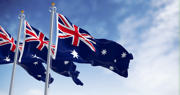 Three Australia national flags waving in the wind on a clear day. Blue flag with Union Jack, white 5-pointed star symbolizing Southern Cross. Rippled fabric. 3D illustration render