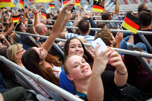 Selfie with german colored flag. Waving flags above large crowd on a stadium sport match. Waiting for the game.