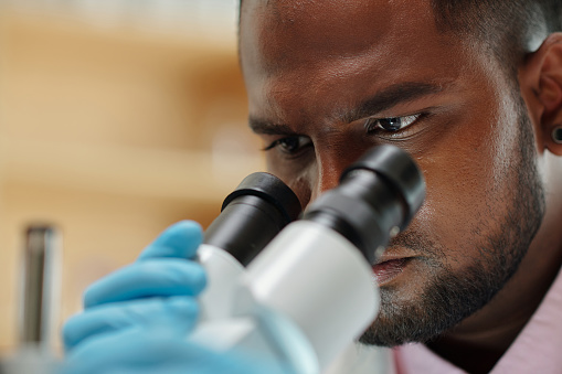 Close-up of face of young scientist or researcher looking in microscope during scientific investigation and study of new substances