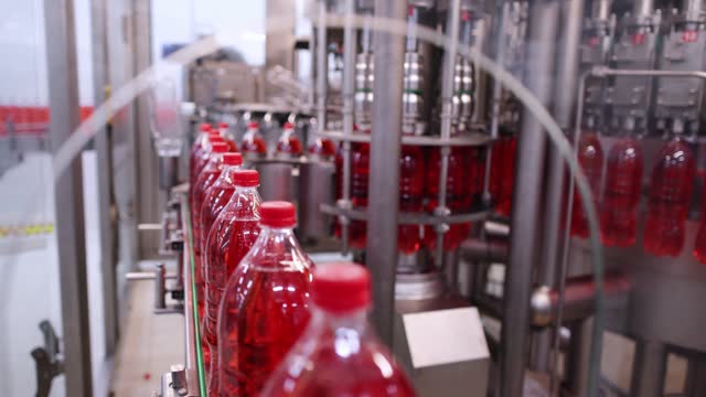 Production line of bottled soda beverage moving on conveyor belt in factory