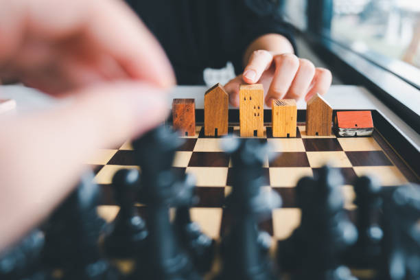 Hand of business man moving chess to Building and house models in chess game, competition success play. strategy, management or leadership concept stock photo