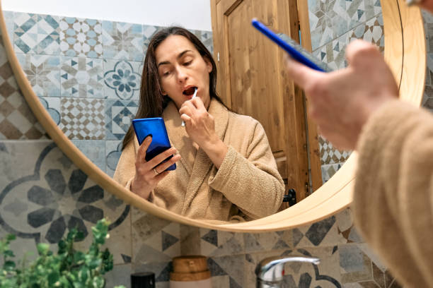 istock Woman brushing teeth with toothbrush and using smartphone for chatting and blogging in front of mirror in bathroom in the morning. Oral hygiene, healthy teeth and care. 1485440589