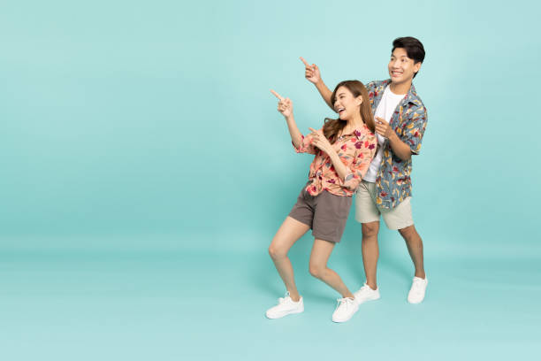 istock Young Asian couple in flower pattern summer outfits pointing to empty copy space isolated on green background 1485441212