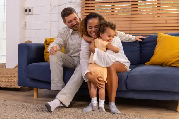 Photo of Happy cheerful parents having fun with cute daughter and hugging on sofa together, Enjoying family lifestyle at home concept