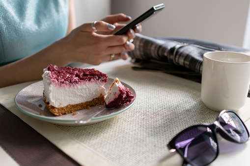 Women siting in caffe looking at cellphone and eating a slice of raspberry cheesecake.