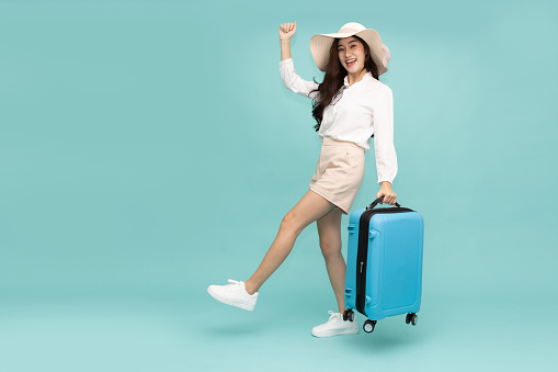 Happy Young Asian traveler woman holding suitcase bag isolated on green background, Tourist in summer and holidays vacation concept