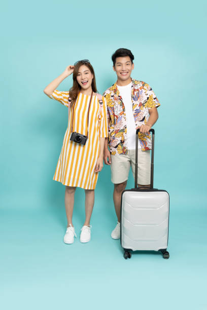 couple asiatique en tenue d’été debout avec sac valise isolé sur fond vert - travel suitcase hawaiian shirt people traveling photos et images de collection