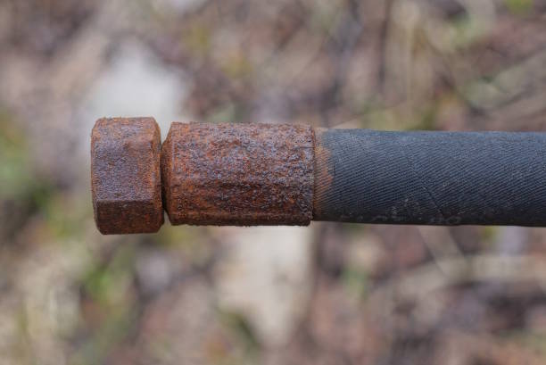 part of an old black plastic hose with a brown rusty iron nut on a gray background outdoors