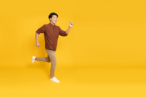 Side view of full length portrait of Asian young businessman walking isolated on yellow background