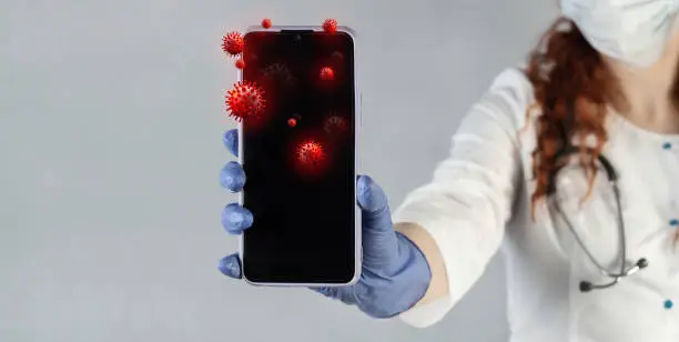Photo of The doctor shows a mobile phone, prevents infection with a virus, germs, bacteria. Smartphone with infectious bacteria and germs on the display.