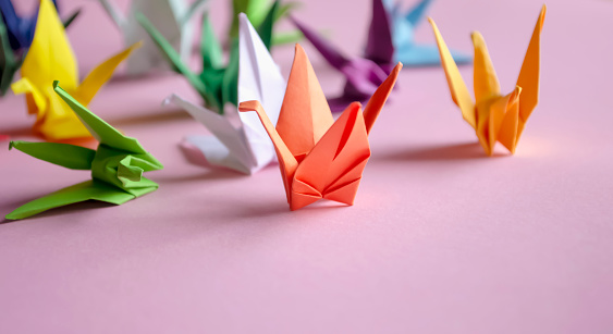 Paper cranes - origami on a pink background. On the table are colored cranes made of paper. cranes on desires. Beautiful paper cranes. Do-it-yourself jewelry.