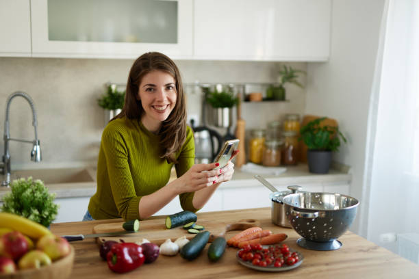 istock Young woman text messaging while cutting vegetables on cutting board in the kitchen 1485456029