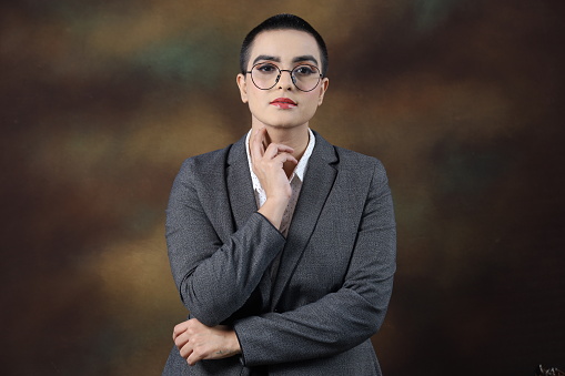 Confident young woman wearing eyeglasses. Portrait of smiling business woman isolated against grey background with copy space. Proud university student girl with specs looking at camera. Short hair wearing specs. Various expressions.