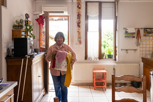 A mature woman who is blind, completing jobs around her home in Castelferrus, France. She is carrying a laundry basket filled with laundry in from the outdoors after it has dried outside in the fresh air.