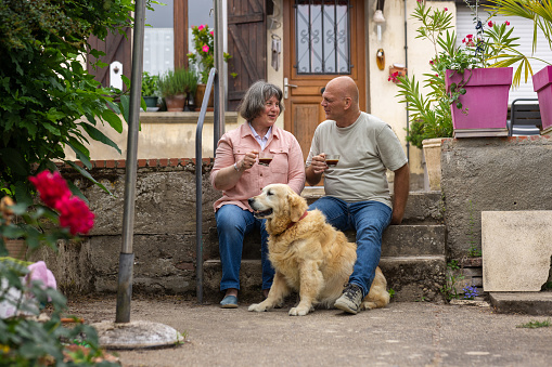 A married couple sitting on steps in their back yard outside their home in Castelferrus, France with their pet golden retriever. They are enjoying a morning coffee while they talk ad connect with each other. The woman is blind.