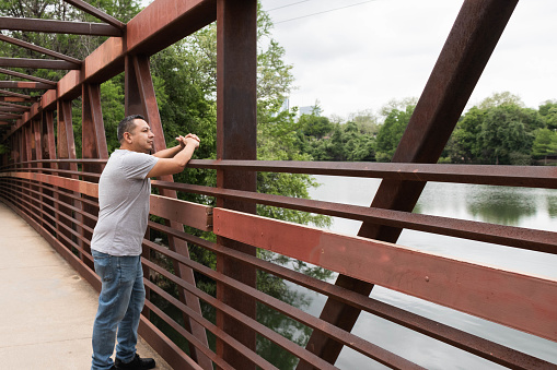 A hispanic man looks out at Lady Bird Lake in Austin, TX from a foot bridge