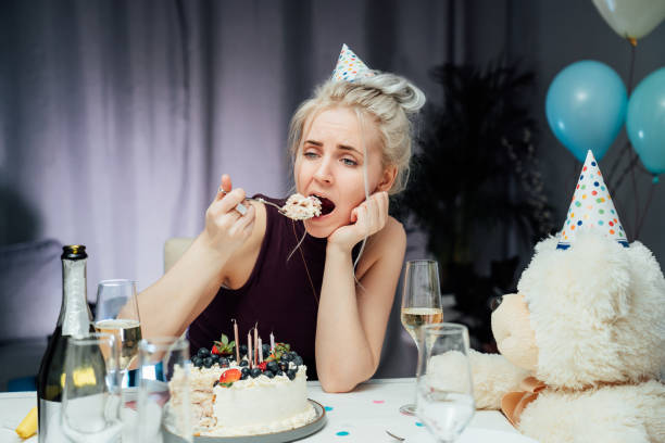 zdenerwowana, nieszczęśliwa atrakcyjna kobieta jedząca świąteczne ciasto podczas świętowania urodzin w domu, siedząca samotnie przy serwowanym stole, odwracająca wzrok, śniąca. selfparty, znudzona impreza. selektywne ustawianie ostrości. - women celebration wine party zdjęcia i obrazy z banku zdjęć