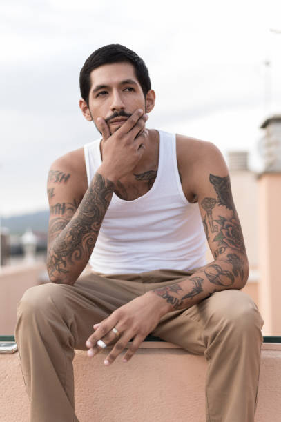 Latin tattooed man sitting on an urban terrace Portrait of a latin man full of tattoos sitting on an urban terrace arm tattoo ideas for men pictures stock pictures, royalty-free photos & images