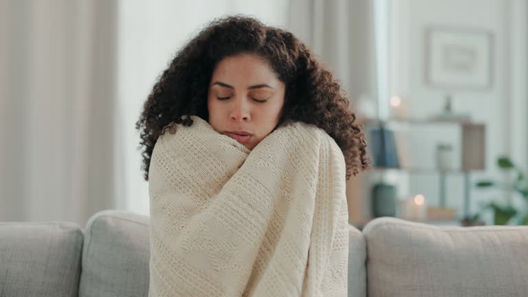 Cold, winter and woman with blanket on sofa for warmth, shivering virus and freezing weather. Sick girl, flu and freeze on couch with body hypothermia, medical illness and fever chills in living room