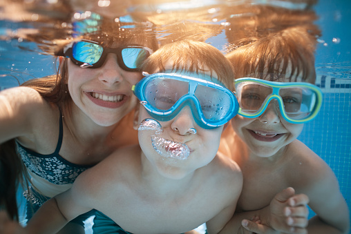 Brothers and sister are having fun playing underwater in the resort pool. Kids are aged 11 and 6.\nNikon D810