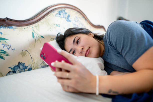 istock Young woman using mobile phone lying on her bed at home 1485474297