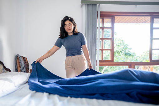 Young woman folding her bedding on the bed in morning at home