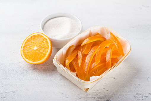 Wicker birch basket with fresh juicy candied oranges with fresh juicy orange and sugar on a light gray background