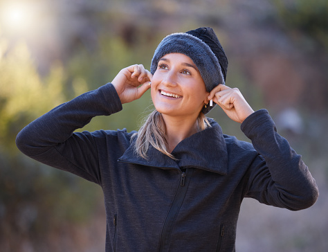 Music, earphones and woman hiking in nature outdoors for health, exercise and fitness. Winter sports, thinking and happy female hiker streaming radio, podcast or audio after training in forest park.