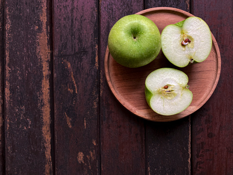 High angle view of ripe fresh organic green apple fruit on a wooden plate over rustic table in the kitchen at home.