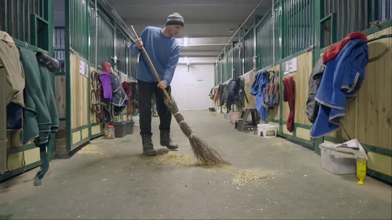 Male stable worker is sweeping the floor.