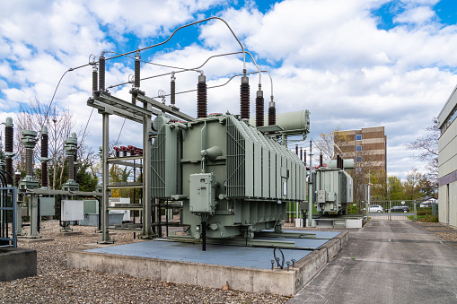 A large stationary electrical transformer on a concrete foundation against a cloudy sky.