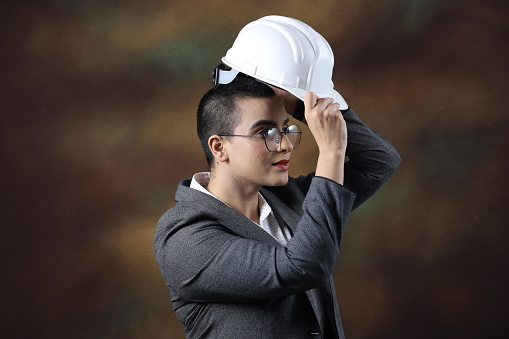 Confident young woman wearing construction helmet. Portrait of smiling business woman isolated against background with copy space. Proud professional engineer looking at camera. Short hair wearing specs. Various expressions.