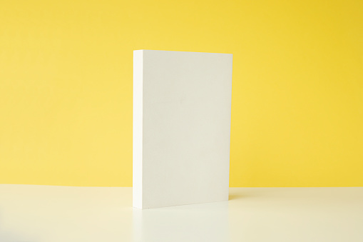 Front view of white blank book on white table in front of  yellow background.